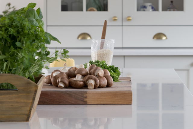 A chef’s table topped with a chopping board, mushrooms and herbs